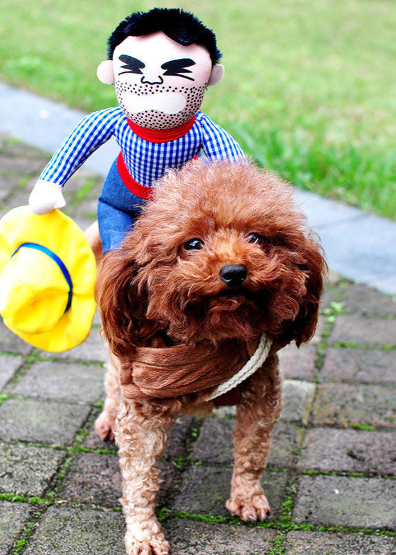 Small brown dog wearing Halloween pet costume with cowboy doll and yellow hat accessory outdoors on paved path